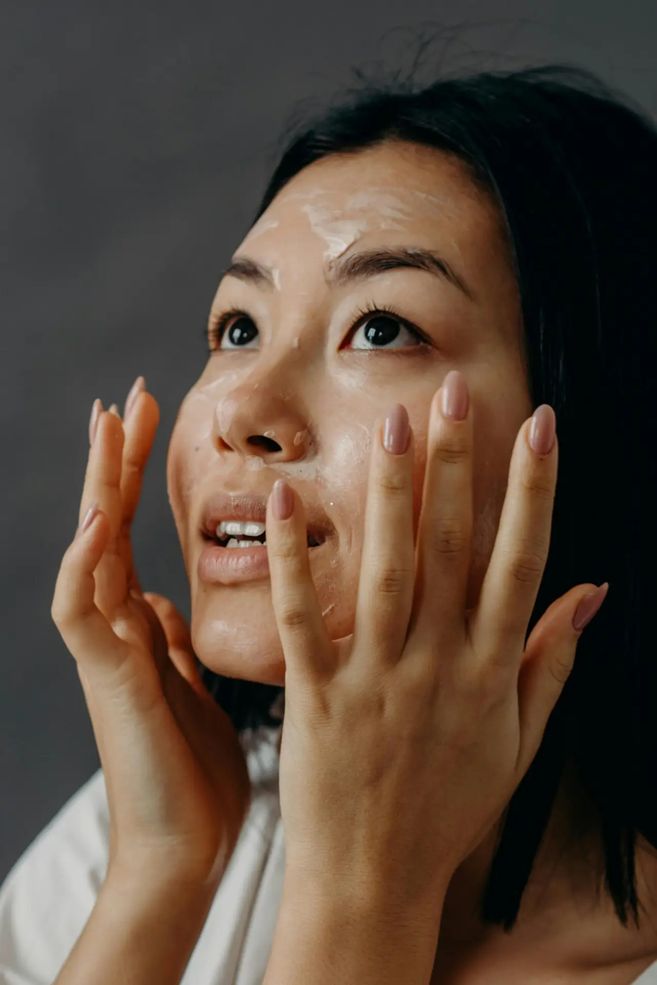 Asian woman applying moisturizer in studio setting for healthy skin.
