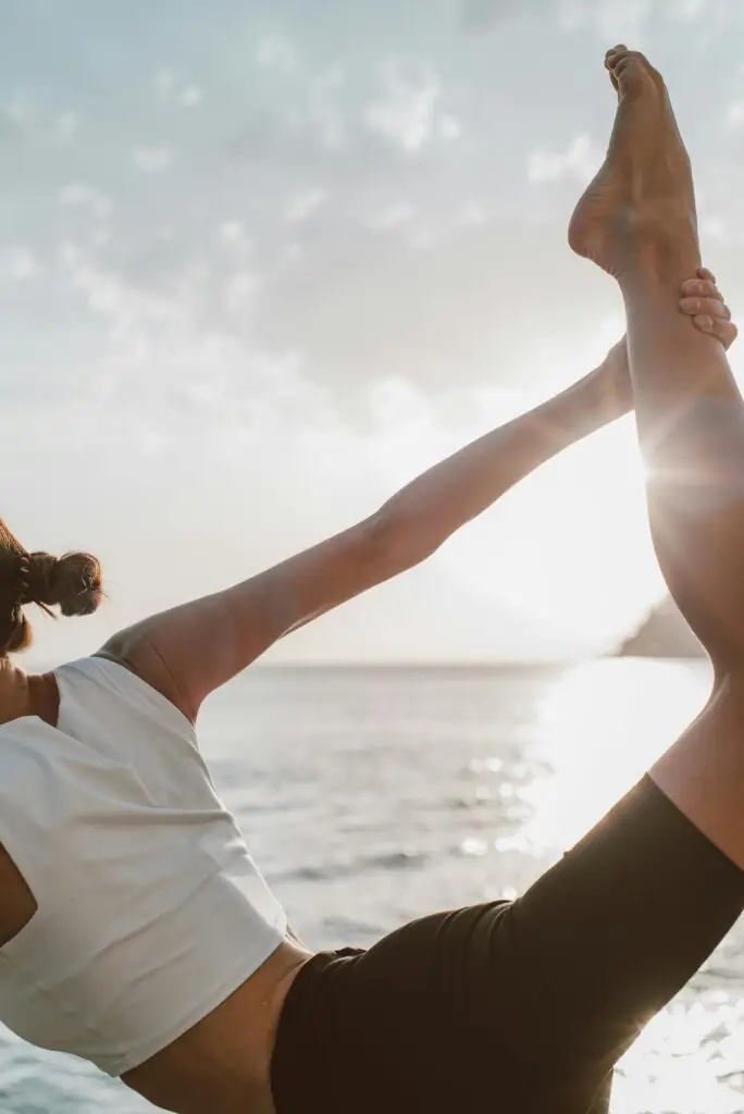 A woman in a yoga pose at sunset by the ocean, embracing wellness and tranquility.